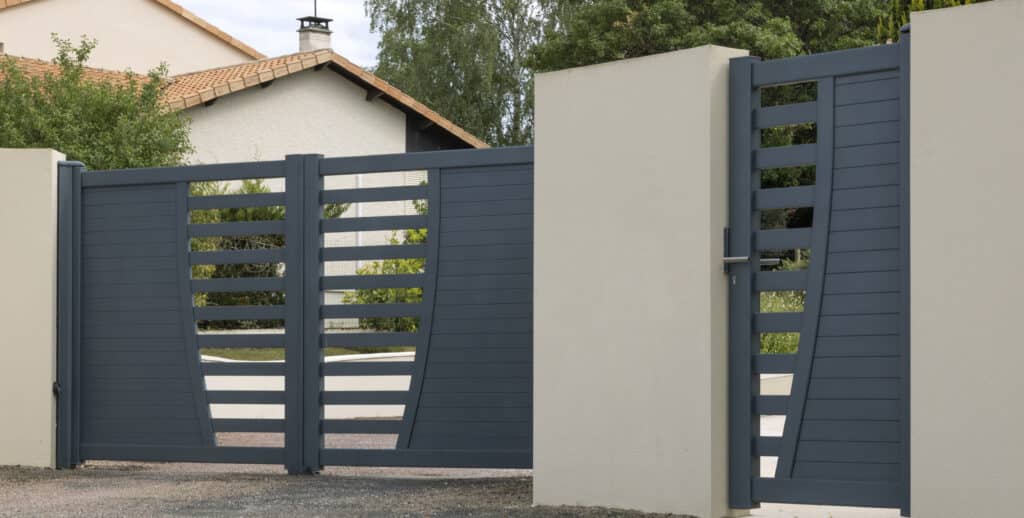 Grand portail coulissant en aluminium gris anthracite avec portillon intégré, design moderne ajouré, devant une entrée de maison.
