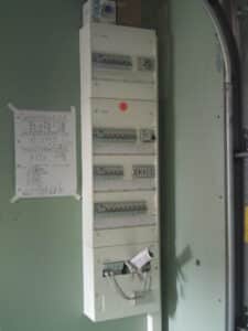 Tableaux électriques Hager empilés avec disjoncteurs et prise, plus un panneau réseau RJ45. Schéma manuscrit des circuits (10A, 16A, 20A, Four, Plaques) sur mur vert.